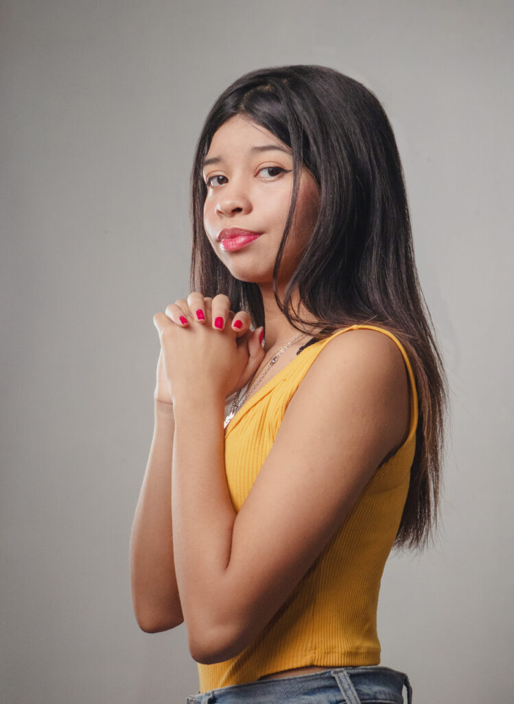 Una imagen de una chica de cabello negro con un top amarillo y jeans azules, en una pose como rezando. La uso como forma de mostrar mi trabajo de fotografo.